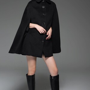 May include: A black wool cape with a collar and button fastening. The cape is being modelled by a woman with blonde hair and black boots.