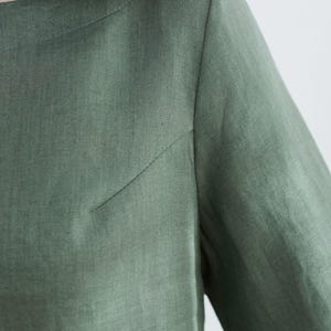 May include: A close-up of a green linen shirt with a round neckline and long sleeves.