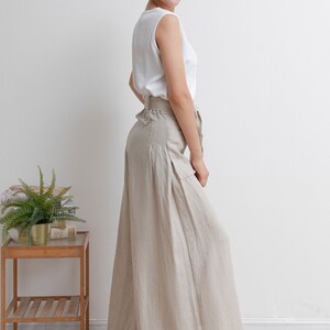May include: A woman wearing a white sleeveless top and beige linen wide-leg pants with a belt. The pants have pleats and a relaxed fit.