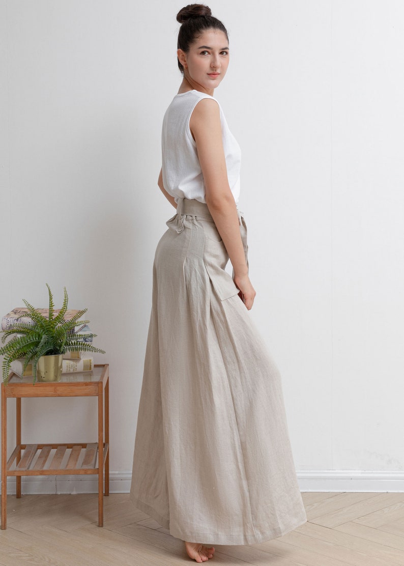 May include: A woman wearing a white sleeveless top and beige linen wide-leg pants with a belt. The pants have pleats and a relaxed fit.