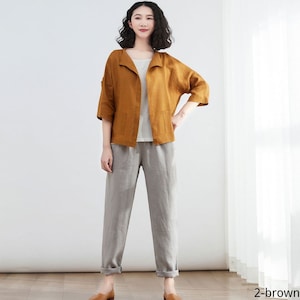 Pode incluir: Uma jaqueta de linho marrom com gola e bolsos, usada sobre uma blusa branca e cal&ccedil;as de linho cinza.