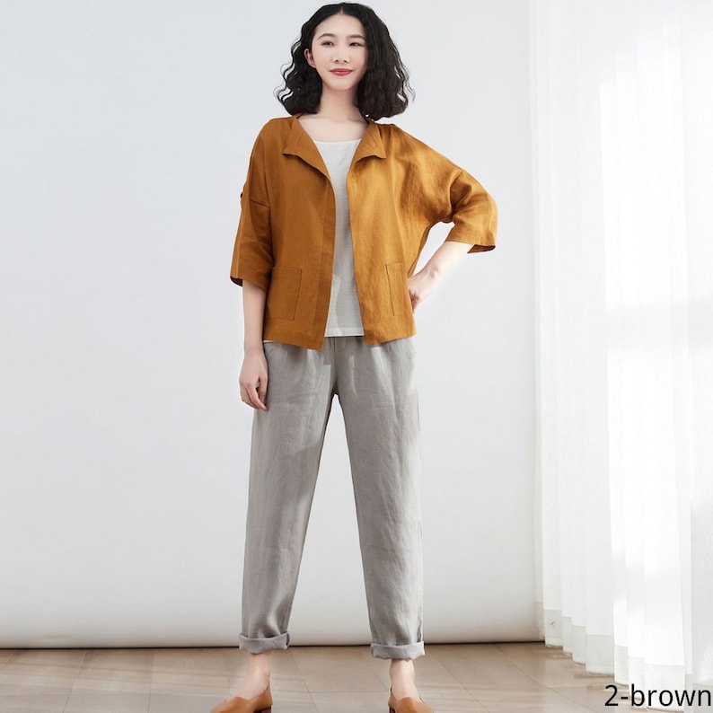 Pode incluir: Uma jaqueta de linho marrom com gola e bolsos, usada sobre uma blusa branca e cal&ccedil;as de linho cinza.