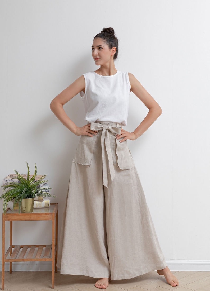 May include: A woman wearing a white sleeveless top and beige linen wide-leg pants with a matching fabric belt tied in a bow at the waist.