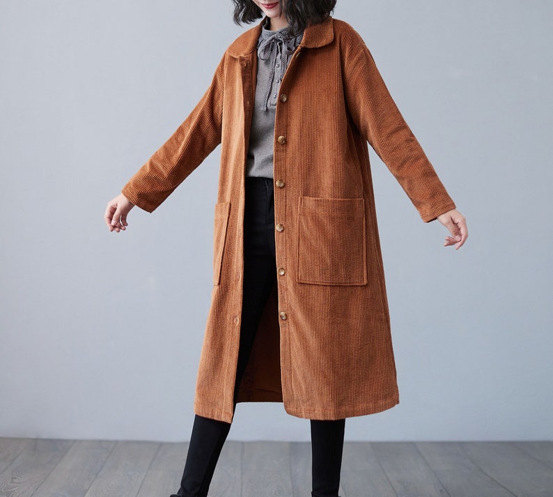 Pu&ograve; includere: Un lungo cappotto di velluto a coste marrone con chiusura a bottoni e due tasche a toppa. Il cappotto ha un colletto e maniche lunghe.