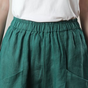 May include: A close-up of a teal green skirt with an elastic waistband and two front pockets. The skirt is made of a lightweight fabric and is paired with a white top.