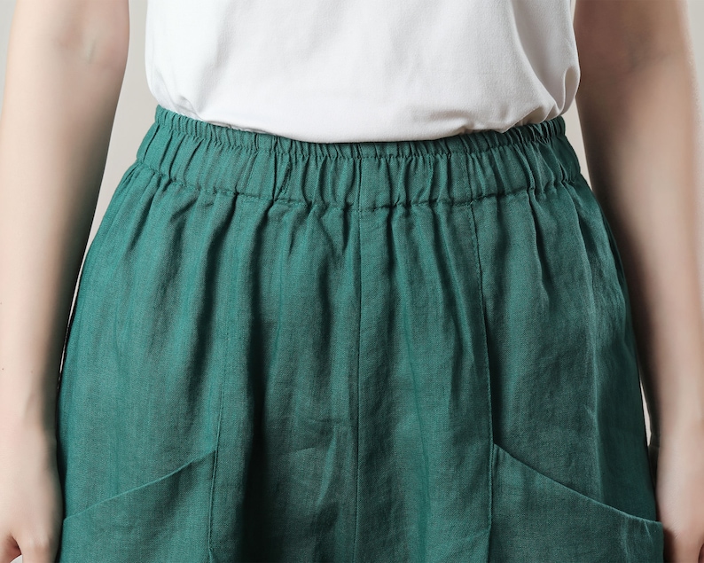 May include: A close-up of a teal green skirt with an elastic waistband and two front pockets. The skirt is made of a lightweight fabric and is paired with a white top.
