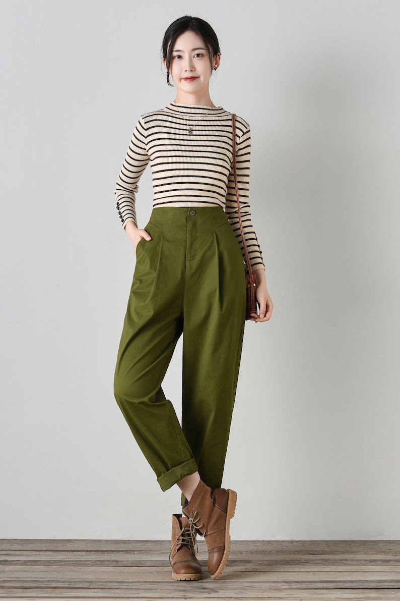 Op de afbeelding: Een vrouw draagt een gestreept shirt met lange mouwen en een groene broek met hoge taille. Ze draagt ​​bruine enkellaarsjes en draagt ​​een bruine tas.