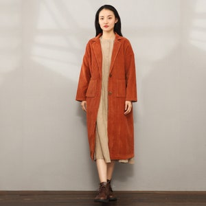 May include: A long, rust-colored corduroy coat with a button closure and two pockets. The coat has a classic, tailored look and is perfect for fall or winter.