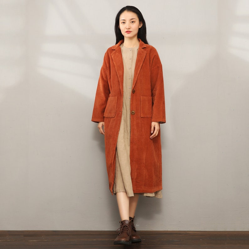 May include: A long, rust-colored corduroy coat with a button closure and two pockets. The coat has a classic, tailored look and is perfect for fall or winter.