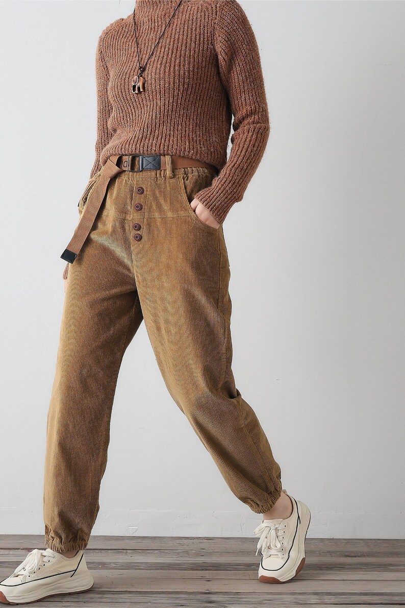 K&ouml;nnte beinhalten: Eine Person tr&auml;gt eine braune Cordhose mit Knopfleiste und einen braunen Strickpullover. Die Hose hat einen G&uuml;rtel mit Schnalle und der Pullover eine Halskette mit Anh&auml;nger.