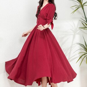 May include: A red midi dress with a v-neckline, button-up front, and short sleeves with ties at the cuffs. The dress has a fitted bodice and a full skirt.