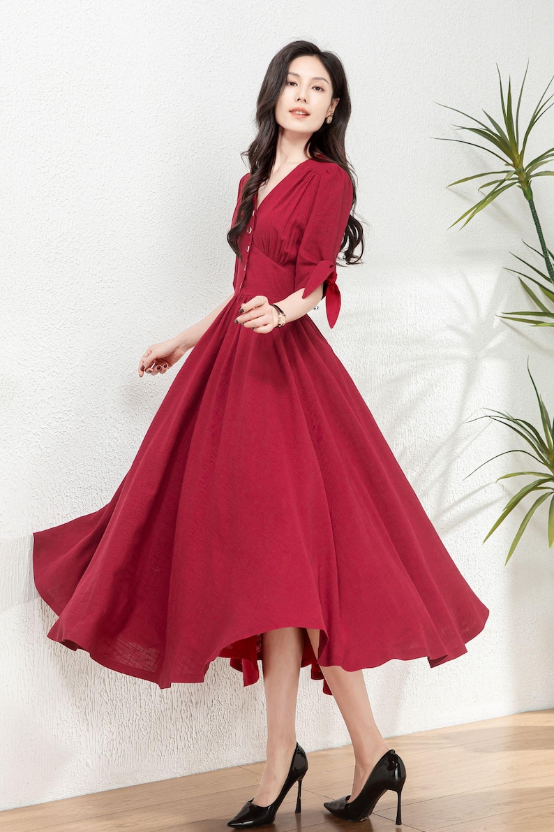 May include: A red midi dress with a v-neckline, button-up front, and short sleeves with ties at the cuffs. The dress has a fitted bodice and a full skirt.