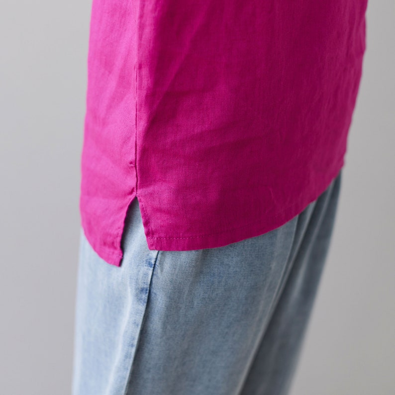 May include: A close-up of a magenta-colored linen shirt with a side slit. The shirt is paired with light blue denim pants. The fabric appears soft and slightly textured, suggesting a casual style.
