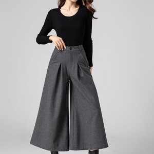 Pu&ograve; includere: Pantaloni larghi a vita alta, di colore grigio, con pieghe. I pantaloni sono realizzati in un tessuto morbido e testurizzato.