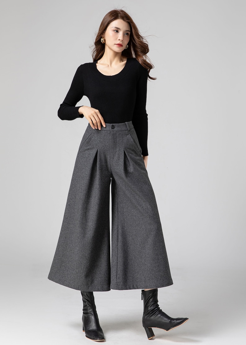 Pu&ograve; includere: Pantaloni larghi a vita alta, di colore grigio, con pieghe. I pantaloni sono realizzati in un tessuto morbido e testurizzato.