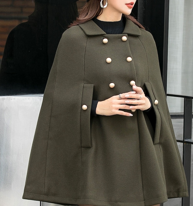 May include: A dark green double-breasted cape with gold buttons. The cape has a collar and long sleeves.