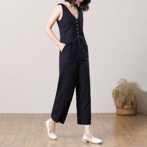 May include: A black sleeveless top with a V-neck and button closure, paired with wide-leg black trousers. The outfit is made of a lightweight fabric and has a relaxed fit.