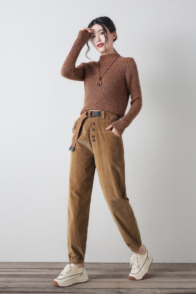 K&ouml;nnte beinhalten: Ein brauner Rollkragenpullover mit einer braunen Cordhose und wei&szlig;en Turnschuhen. Die Hose hat einen braunen G&uuml;rtel und Knopfdetails.