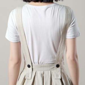 May include: A white linen overall dress with adjustable straps and a simple, classic design. The dress has a relaxed fit and is perfect for casual wear.