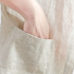 Pode incluir: Um close-up de um colete de linho bege com um bolso grande na frente. O bolso tem uma aba e &eacute; costurado com uma linha bege contrastante.