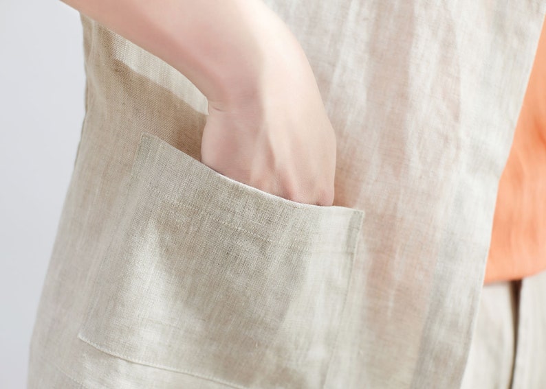 Pode incluir: Um close-up de um colete de linho bege com um bolso grande na frente. O bolso tem uma aba e &eacute; costurado com uma linha bege contrastante.