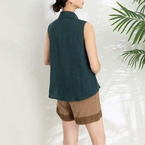 May include: A sleeveless, dark green linen shirt with a collared neckline. The shirt is paired with brown shorts that have a lace trim.