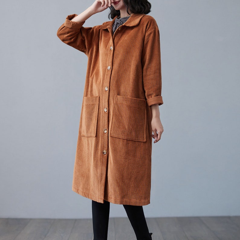 Pu&ograve; includere: Un lungo cappotto di velluto a coste marrone con chiusura a bottoni e due grandi tasche. Il cappotto ha un colletto e maniche lunghe.