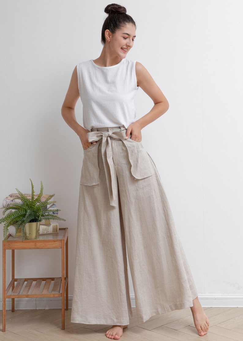 May include: A woman wearing a white sleeveless top and beige linen wide-leg pants with a matching fabric belt. The pants have large patch pockets on the front.