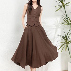 Peut inclure: Un gilet sans manches marron avec des boutons et une jupe &eacute;vas&eacute;e marron assortie. La tenue est en tissu de type lin.