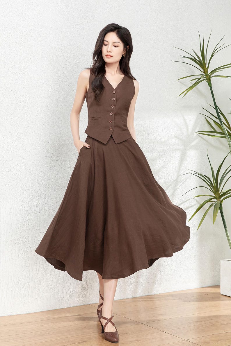 Peut inclure: Un gilet sans manches marron avec des boutons et une jupe &eacute;vas&eacute;e marron assortie. La tenue est en tissu de type lin.