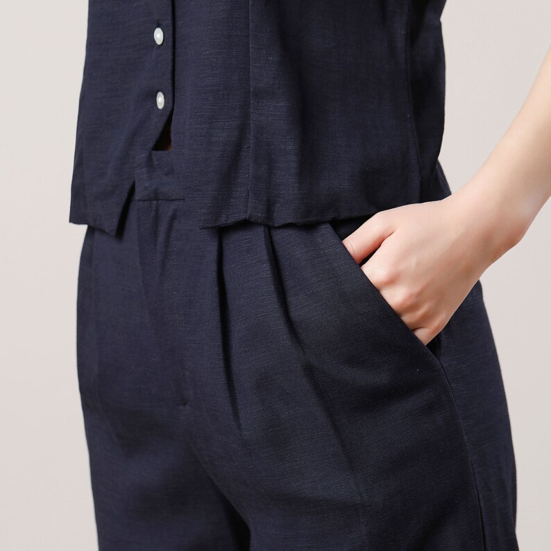 May include: A dark blue linen pantsuit with a button-up top and a front pocket. The trousers have pleats at the front.