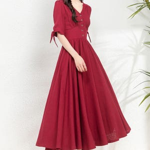 May include: A red midi dress with a v-neckline, short sleeves, and a button-up front. The dress has a fitted bodice and a full skirt.