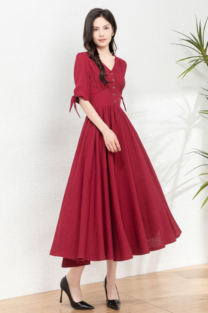 May include: A red midi dress with a v-neckline, short sleeves, and a button-up front. The dress has a fitted bodice and a full skirt.