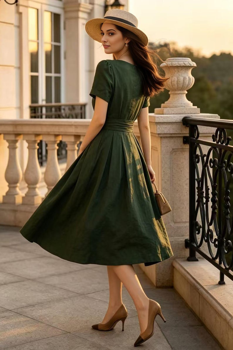 May include: A dark green midi dress with short sleeves, a fitted waist, and a pleated skirt. The dress is paired with a straw hat featuring a black band and tan high-heeled pumps with dark brown pointed toes, while holding a small tan handbag.