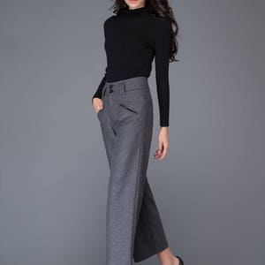 Puede incluir: Una mujer con un su&eacute;ter de cuello alto negro y pantalones grises de pierna ancha. Lleva tacones negros y tiene el pelo largo y oscuro.