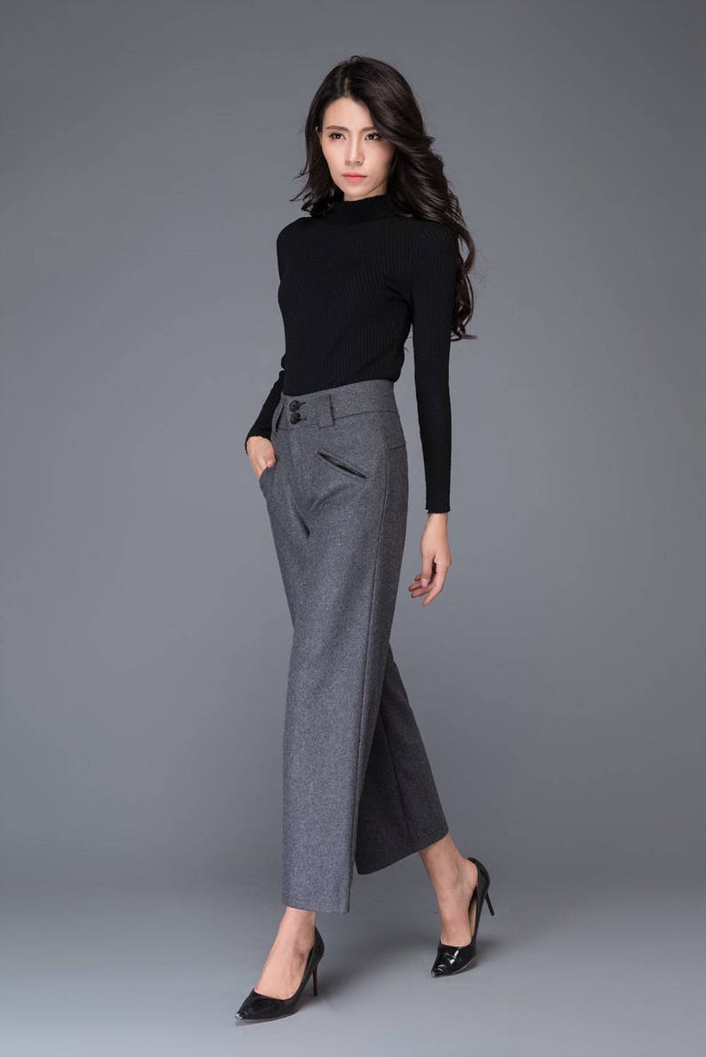 Puede incluir: Una mujer con un su&eacute;ter de cuello alto negro y pantalones grises de pierna ancha. Lleva tacones negros y tiene el pelo largo y oscuro.