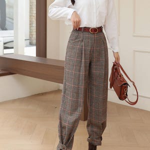 K&ouml;nnte beinhalten: Ein wei&szlig;es Hemd mit Karohose, einem braunen G&uuml;rtel und braunen Lederstiefeln. Die Hose hat ein grau-rot-wei&szlig;es Karomuster. Eine braune Lederhandtasche vervollst&auml;ndigt das Outfit.