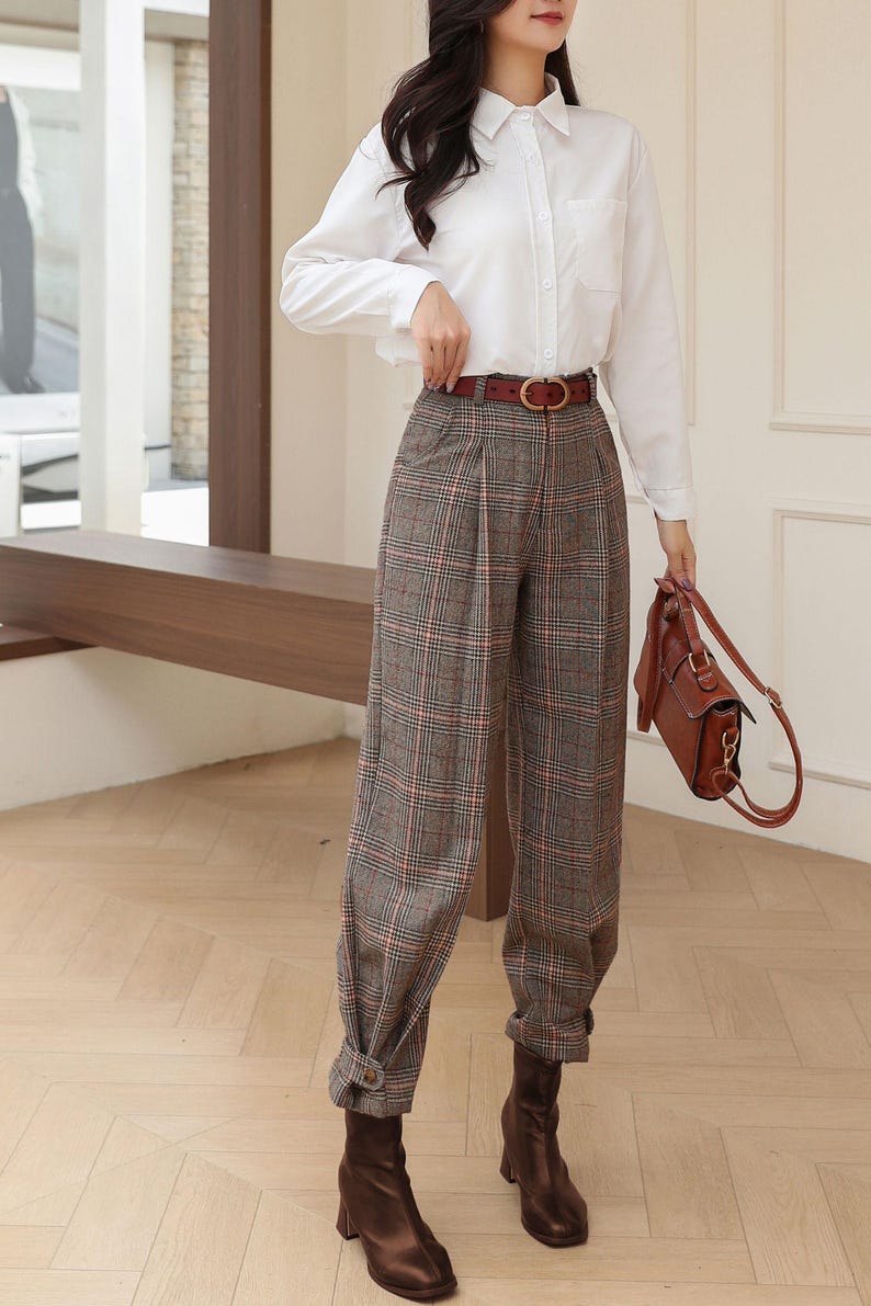 K&ouml;nnte beinhalten: Ein wei&szlig;es Hemd mit Karohose, einem braunen G&uuml;rtel und braunen Lederstiefeln. Die Hose hat ein grau-rot-wei&szlig;es Karomuster. Eine braune Lederhandtasche vervollst&auml;ndigt das Outfit.