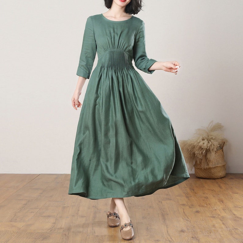 May include: A green linen dress with a round neckline and 3/4 sleeves. The dress has a fitted bodice and a flowing skirt.