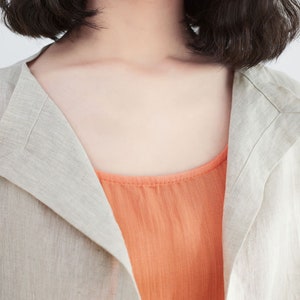 Pode incluir: Uma mulher vestindo uma jaqueta de linho bege claro sobre um top de cor coral.