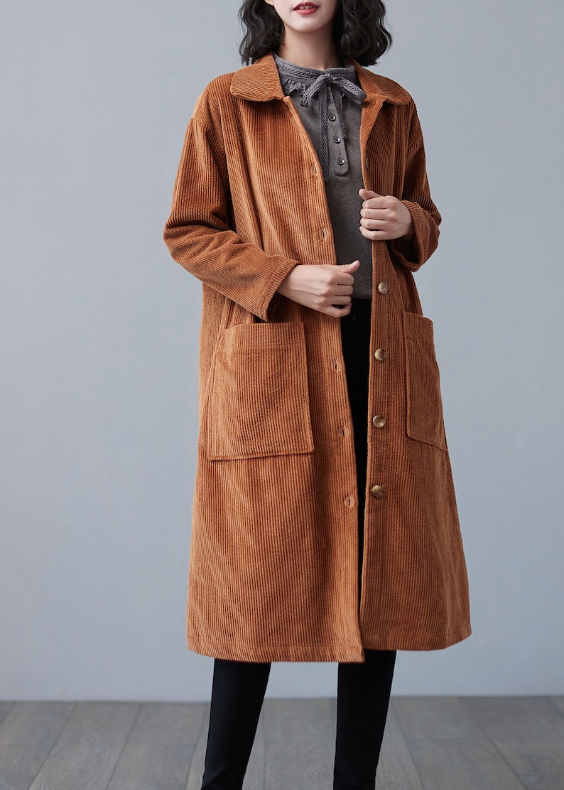 Pu&ograve; includere: Un lungo cappotto di velluto a coste marrone con chiusura a bottoni e due grandi tasche a toppa. Il cappotto ha un colletto e maniche lunghe.