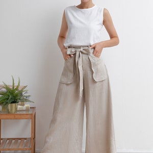 May include: A woman wearing a white sleeveless top and beige linen wide-leg pants with a bow tie at the waist.