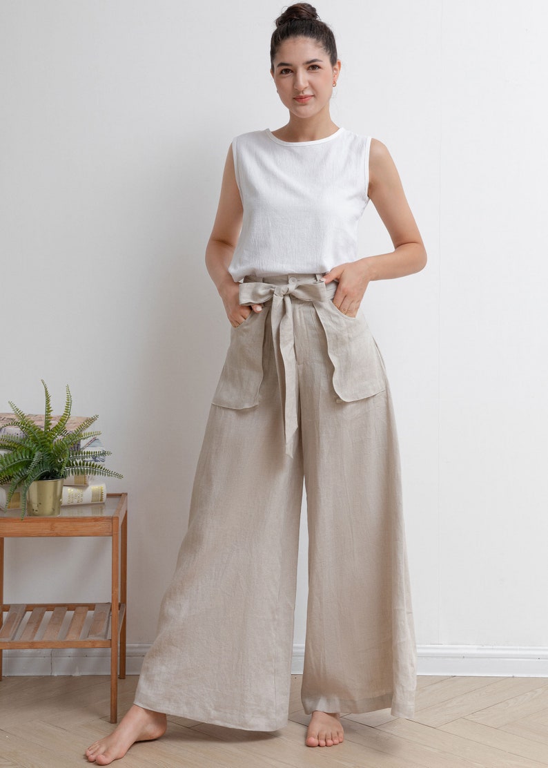 May include: A woman wearing a white sleeveless top and beige linen wide-leg pants with a bow tie at the waist.