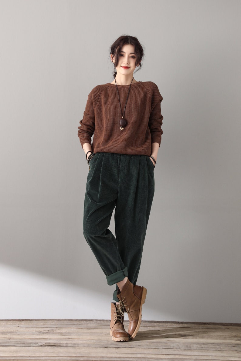 May include: A woman wearing a brown sweater and green corduroy pants. She is wearing brown leather boots and has a necklace with a wooden pendant.