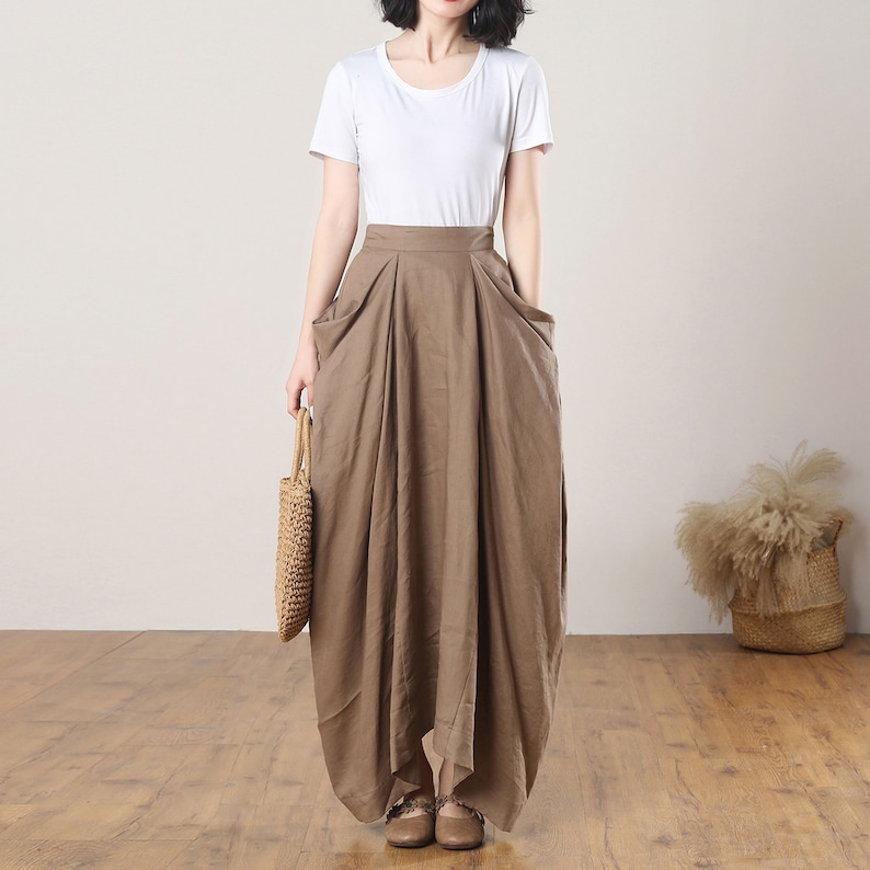 May include: A brown linen maxi skirt with a high waist and pockets. The skirt is pleated and has a loose, flowing fit.