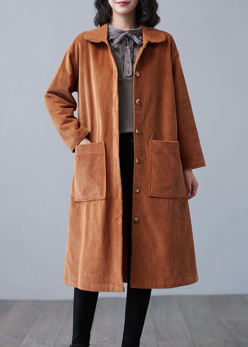 Pu&ograve; includere: Un lungo cappotto di velluto a coste marrone con chiusura a bottoni e due grandi tasche a toppa. Il cappotto ha un colletto e maniche lunghe.