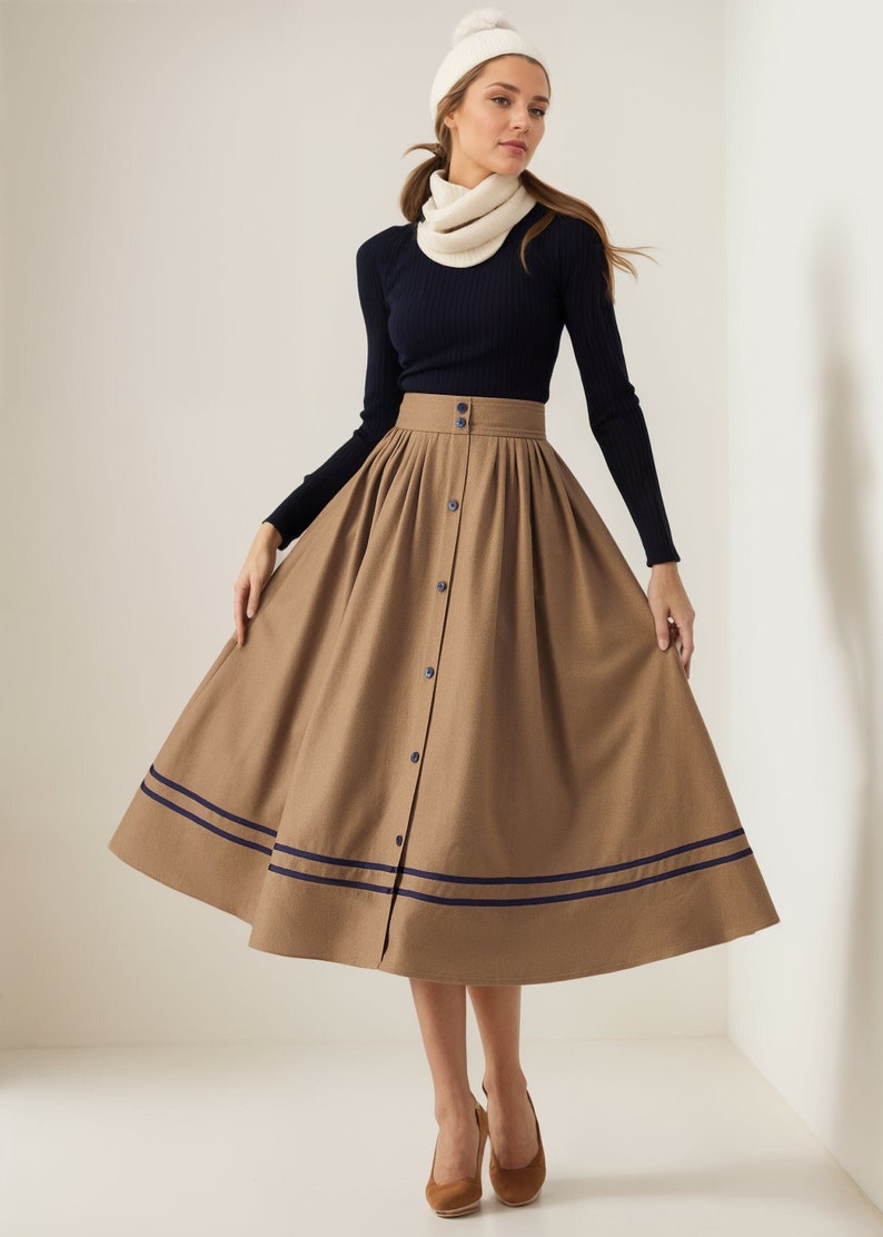 May include: A brown midi skirt with a button-up front and two navy blue stripes around the hem. The skirt is pleated and has a high waist.
