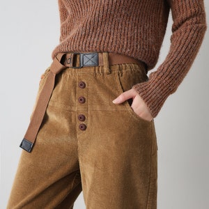 K&ouml;nnte beinhalten: Braune Cordhose mit Knopfleiste und braunem Stoffg&uuml;rtel. Die Hose hat eine lockere Passform und ist aus einem weichen, bequemen Material gefertigt.