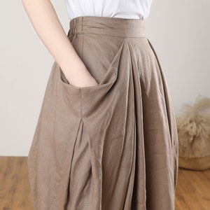 May include: A brown linen skirt with a large pocket on the front. The skirt has a wide waistband and a flowing silhouette.