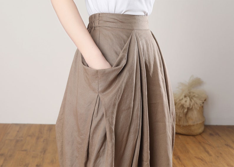 May include: A brown linen skirt with a large pocket on the front. The skirt has a wide waistband and a flowing silhouette.